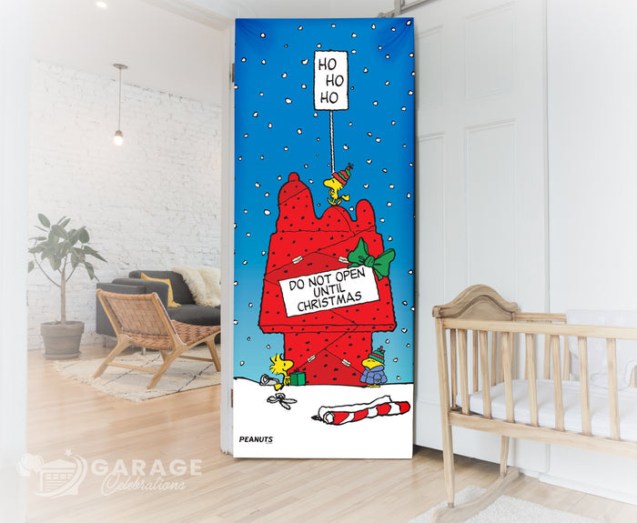 Decorative bedroom door with Christmas-themed design featuring Snoopy and other Peanuts characters on top of a a red dog house wrapped up like a gift and sign that reads "Do not open until Christmas."