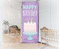 Decorative birthday banner with cake and candles in a room with a crib and plant.