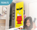 Girl reading a book in front of a Snoopy door cover in a room with 'Peanuts' branding.