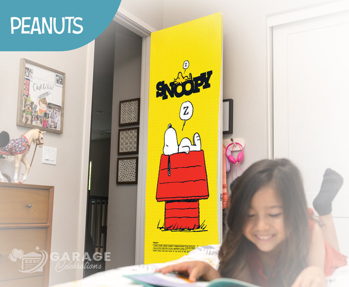 Girl reading a book in front of a Snoopy door cover in a room with 'Peanuts' branding.